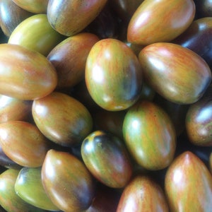 May include: A close-up of a pile of heirloom tomatoes. The tomatoes are a mix of green, brown, and purple, with a mottled appearance.