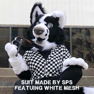 May include: A black and white furry fursuit with a checkerboard shirt and a camera. The fursuit has large, expressive eyes and a dog-like snout. The text on the image reads "SUIT MADE BY SPS FEATURING WHITE MESH."