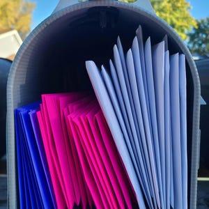 May include: A mailbox full of envelopes. The envelopes are stacked in a fan shape. The envelopes are white, pink, and blue.