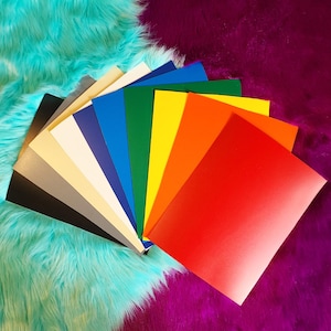 May include: A fan of colorful cardstock paper in various shades, including red, orange, yellow, green, blue, and black. The papers are arranged on a turquoise and purple faux fur background.