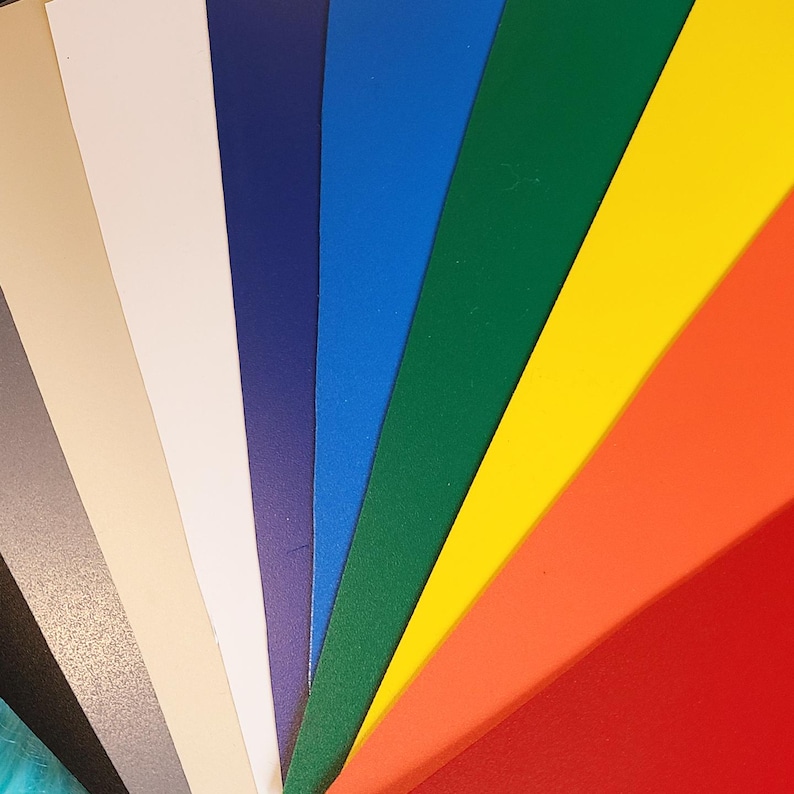 May include: A fan of colorful paper sheets in various shades, including gray, beige, white, navy, blue, green, yellow, orange, and red. The sheets are arranged to display a spectrum of colors.