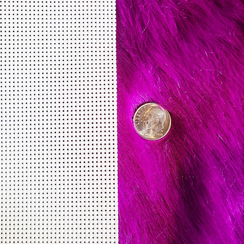 May include: A close-up shot features a dime coin on a vibrant, fuchsia-colored, faux fur surface. To the left, a white plastic canvas with evenly spaced square holes is visible. The coin is approximately 0.7 inches in diameter.