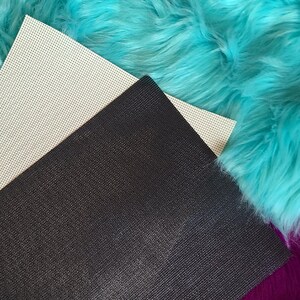 May include: Close-up of craft supplies featuring a black, textured sheet, a cream-colored sheet with small holes, and vibrant turquoise faux fur. The materials are arranged diagonally, showcasing their textures and colors.