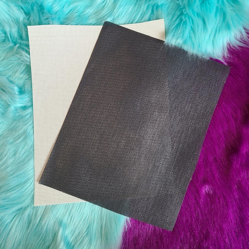 May include: Two rectangular sheets of craft material. One is off-white with a grid of small holes, the other is dark gray with a textured surface. The sheets are layered on a background of turquoise and purple faux fur.