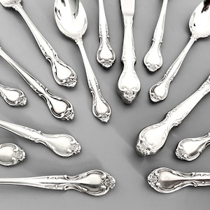 May include: A set of silver flatware with ornate handles, including forks, knives, and spoons.