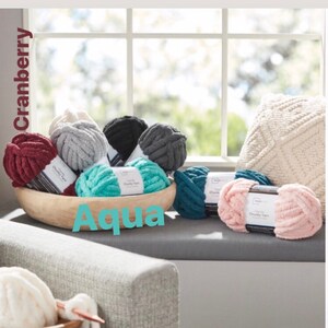 May include: A variety of chunky yarn in different colors, including cranberry, aqua, gray, and pink. The yarn is displayed in a wooden bowl and on a windowsill.
