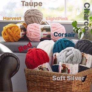 May include: A basket filled with various colors of chunky yarn, including taupe, harvest, light pink, red, soft silver, charcoal, and corsair. The yarn is arranged in a circle around the basket.