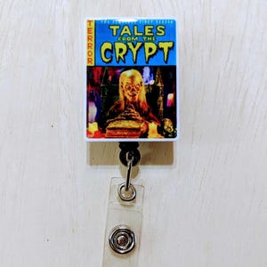 May include: A Tales From The Crypt retractable badge reel. The reel features a rectangular design with the show's title in yellow and blue, and an image of a ghoul. The word "TERROR" is printed vertically on the left side.