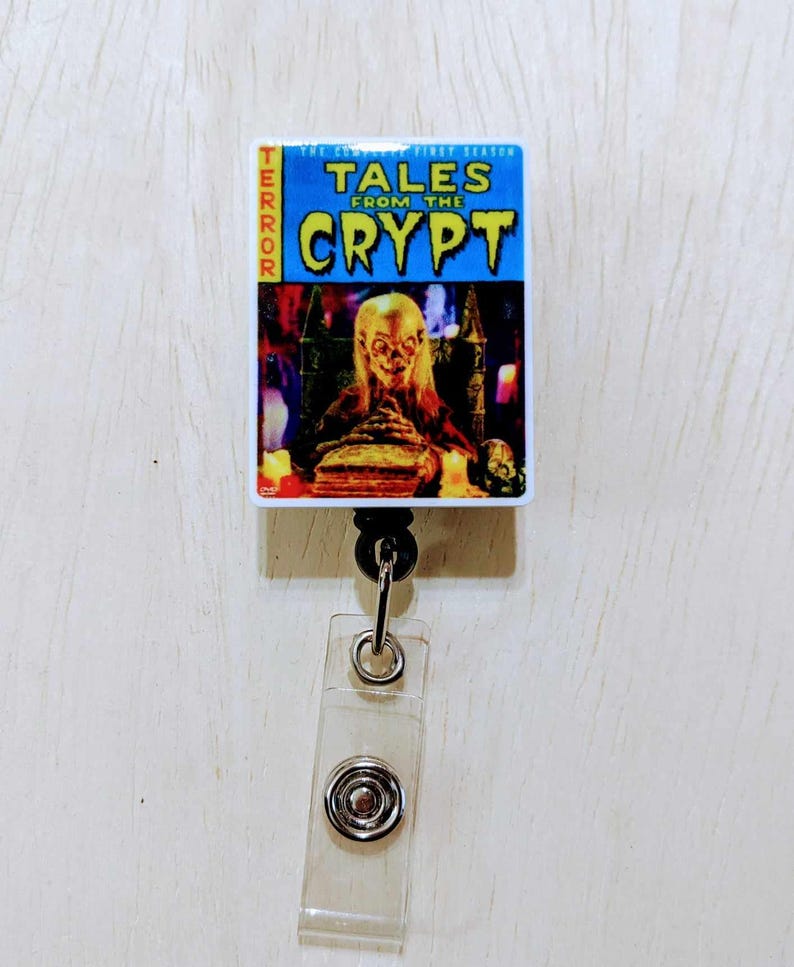 May include: A Tales From The Crypt retractable badge reel. The reel features a rectangular design with the show's title in yellow and blue, and an image of a ghoul. The word "TERROR" is printed vertically on the left side.