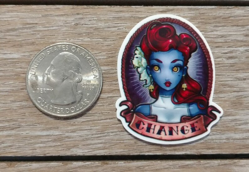 May include: A sticker featuring a blue-skinned woman with red hair and yellow eyes. She is wearing a white dress and has a skull earring. The sticker has a banner that says "CHANGE" in red and white letters.