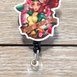 May include: A white and red retractable badge holder with a cartoon image of a woman with red hair and green clothing. The image has the text "Can't Touch This" around it.