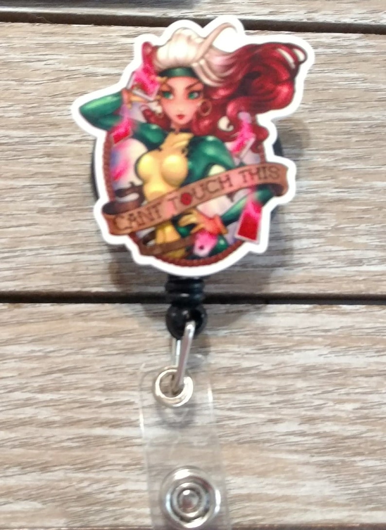 May include: A white and red retractable badge holder with a cartoon image of a woman with red hair and green clothing. The image has the text "Can't Touch This" around it.