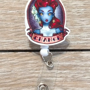 May include: A white retractable badge holder with a round, colorful graphic featuring a woman with red hair and blue skin. The graphic has the word "CHANGE" written on a banner.