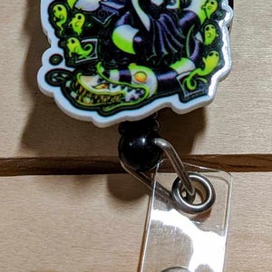 May include: A retractable badge reel featuring a colorful graphic of a character with green hair and a black and white striped snake. The reel has a clear plastic strap and a metal snap.