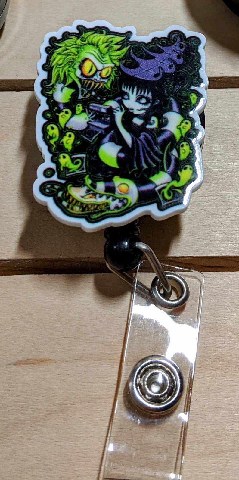 May include: A retractable badge reel featuring a colorful graphic of a character with green hair and a black and white striped snake. The reel has a clear plastic strap and a metal snap.