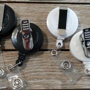 May include: Four retractable badge holders, two black and two white, with a metal clip and a clear plastic strap.