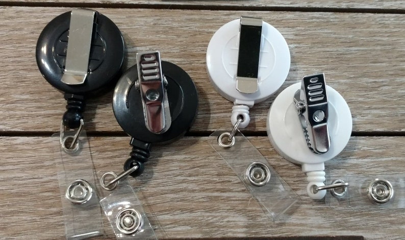 May include: Four retractable badge holders, two black and two white, with a metal clip and a clear plastic strap.