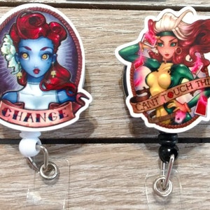 May include: Two colorful cartoon character badge reels. The first reel features a blue-skinned woman with red hair and the text "CHANGE". The second reel features a woman with green and yellow clothing and the text "CANT TOUCH THIS".