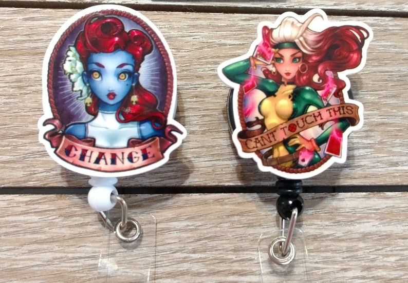 May include: Two colorful cartoon character badge reels. The first reel features a blue-skinned woman with red hair and the text "CHANGE". The second reel features a woman with green and yellow clothing and the text "CANT TOUCH THIS".