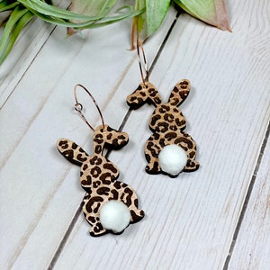 May include: A pair of hoop earrings featuring a leopard print bunny silhouette with a white pom-pom tail.
