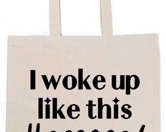 May include: A beige canvas tote bag with black text that reads "I woke up like this #engaged".
