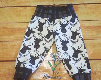 May include: White and black patterned baby trousers with a matching beanie. The trousers have a black and white plaid waistband and the beanie has a black and white plaid band. The pattern features a silhouette of a deer head with antlers.