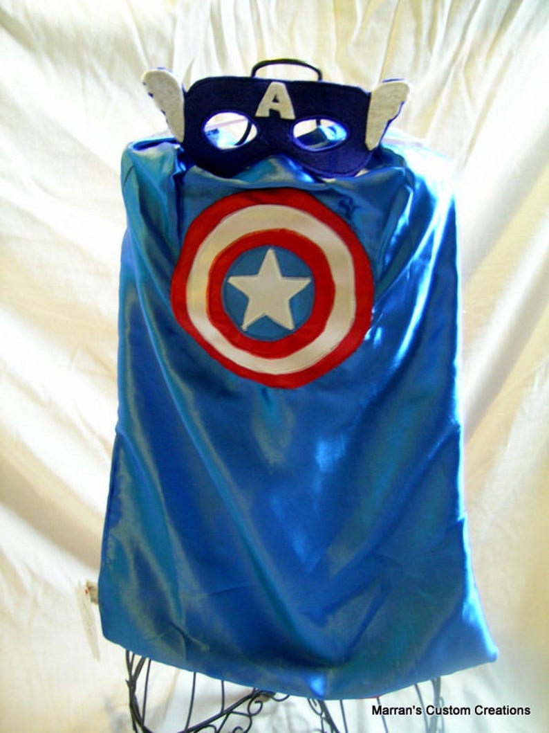May include: A blue satin cape with a red, white, and blue circle design in the center. The cape is topped with a blue felt mask with a white felt star and the letter "A" on the front.
