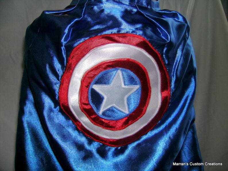 May include: A blue satin cape with a red, white, and blue embroidered circle design. The circle features a white star in the center.