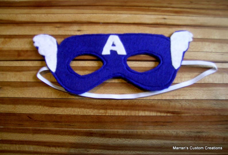 May include: A blue felt mask with a white felt "A" on the front and white felt wings on the sides. The mask has elastic straps.