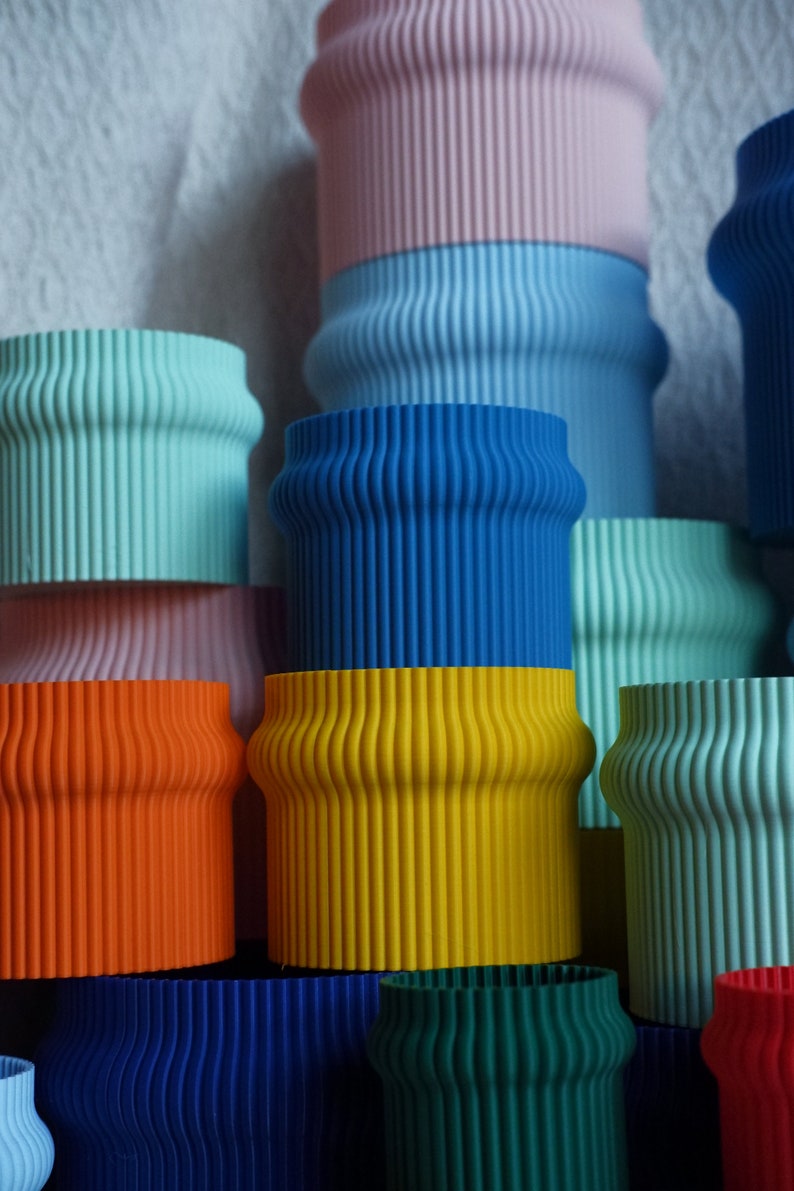 May include: A stack of colorful, ribbed, cylindrical planters in various shades of blue, green, yellow, orange, and pink. The planters are made of a smooth, textured material.