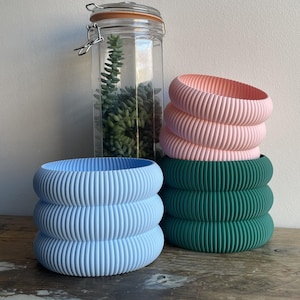 May include: Three stackable plant pots in blue, green, and pink. The pots have a ribbed design and are made of a smooth, matte material.
