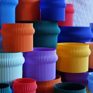 May include: A stack of colorful, ribbed, cylindrical containers in various shades of blue, green, orange, red, yellow, and purple.