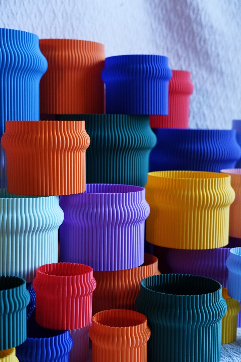 May include: A stack of colorful, ribbed, cylindrical containers in various shades of blue, green, orange, red, yellow, and purple.