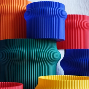 May include: A set of six colorful, cylindrical planters with a ribbed texture. The planters are stacked in a pyramid shape, with the largest planter at the bottom and the smallest planter at the top. The planters are orange, blue, green, blue, yellow, and red.