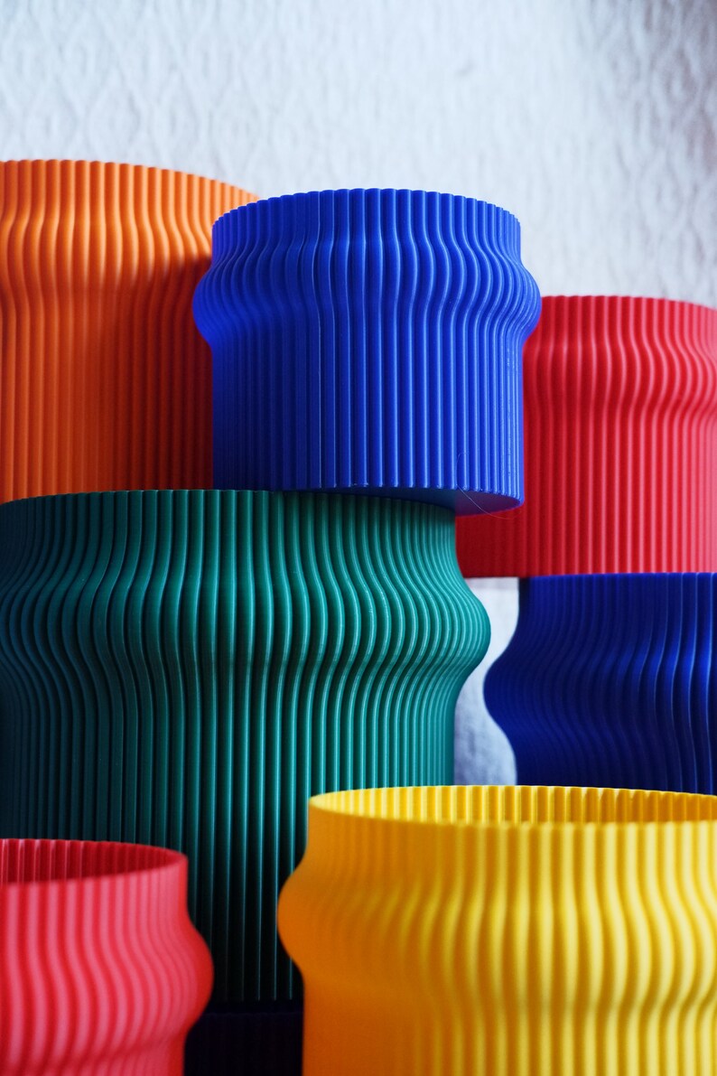 May include: A set of six colorful, cylindrical planters with a ribbed texture. The planters are stacked in a pyramid shape, with the largest planter at the bottom and the smallest planter at the top. The planters are orange, blue, green, blue, yellow, and red.