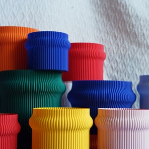 May include: A collection of colorful, wavy-edged, cylindrical planters in various shades of blue, green, yellow, red, and pink. The planters are stacked and arranged in a pyramid shape.