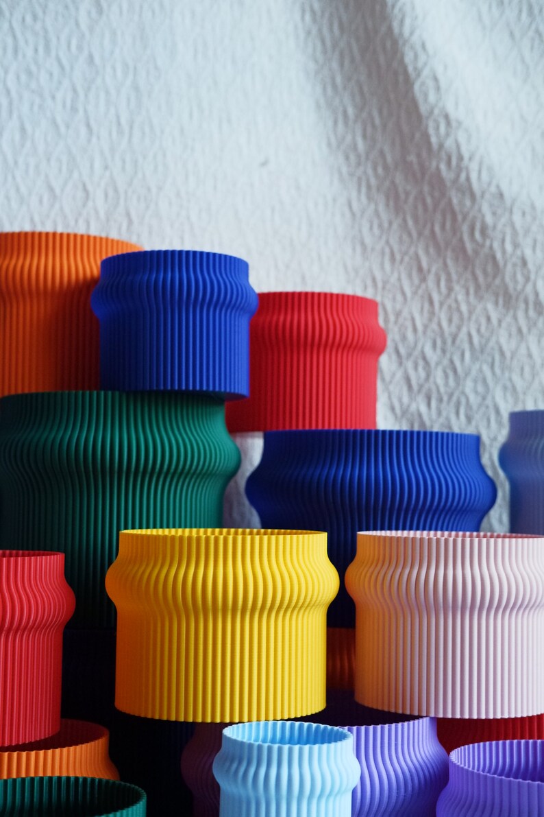 May include: A collection of colorful, wavy-edged, cylindrical planters in various shades of blue, green, yellow, red, and pink. The planters are stacked and arranged in a pyramid shape.