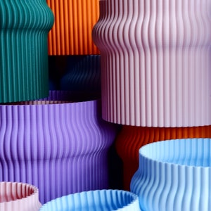May include: A collection of colorful, ribbed, ceramic planters in various sizes. The planters are stacked and arranged in a visually appealing way, showcasing their unique texture and vibrant hues.