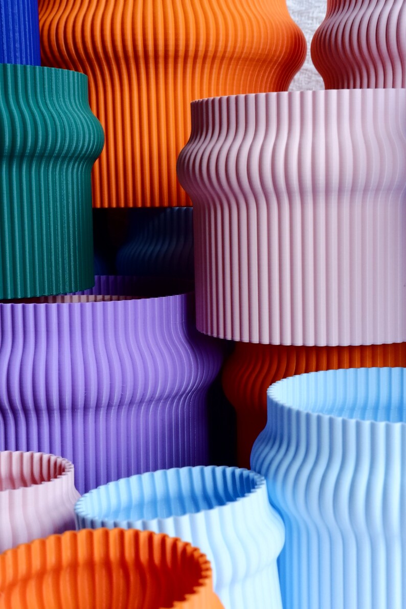 May include: A collection of colorful, ribbed, ceramic planters in various sizes. The planters are stacked and arranged in a visually appealing way, showcasing their unique texture and vibrant hues.
