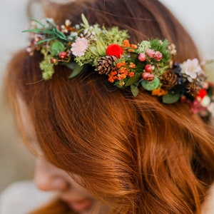 May include: A woman with long, red hair wearing a floral crown with red berries, pine cones, and green leaves.