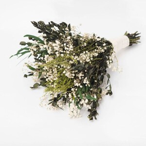 May include: A bouquet of dried flowers with dark green leaves, tiny white flowers, and light green sprigs. The stems are bound with a cream-coloured ribbon, creating a natural and elegant arrangement.