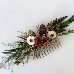 May include: A gold hair comb decorated with dried flowers and pine cones. The flowers are white and the pine cones are brown.
