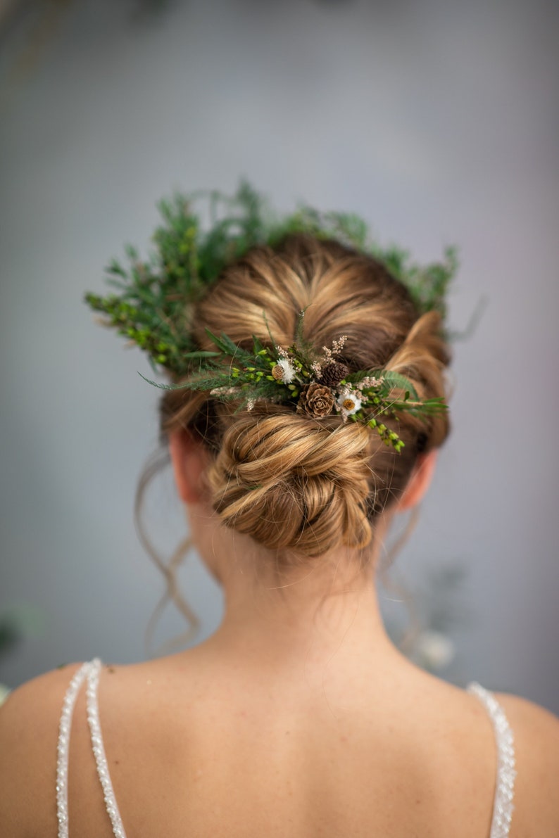 May include: A woman with blonde hair styled in a bun with a green and brown floral crown.