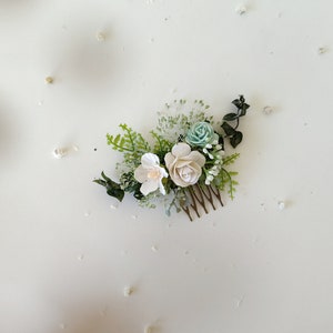 Peut inclure: Un peigne à cheveux floral blanc et bleu clair avec des feuilles vertes. Le peigne est en métal et a un design décoratif.