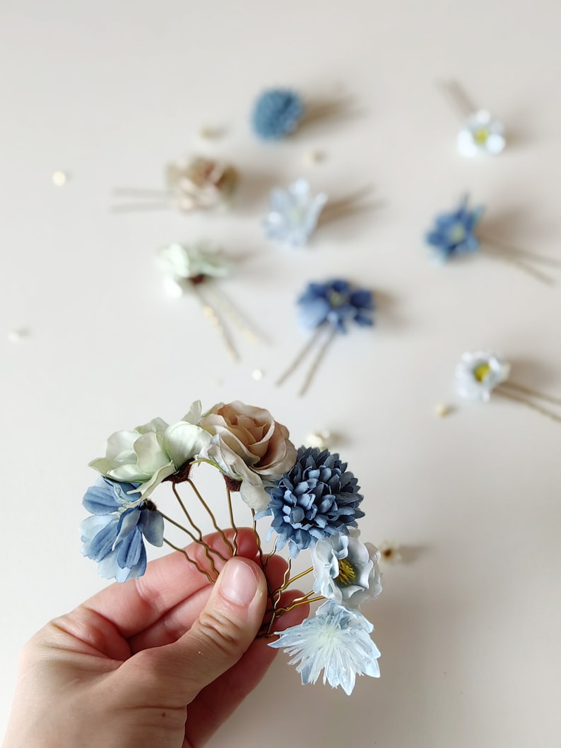 K&ouml;nnte beinhalten: Blumen-Haarnadeln in verschiedenen Blau-, Gr&uuml;n- und Beiget&ouml;nen. Die Haarnadeln haben Stoffblumen und sind auf goldfarbenen Metall-Haarnadeln angebracht. Der Hintergrund ist eine weiche, neutrale Farbe.