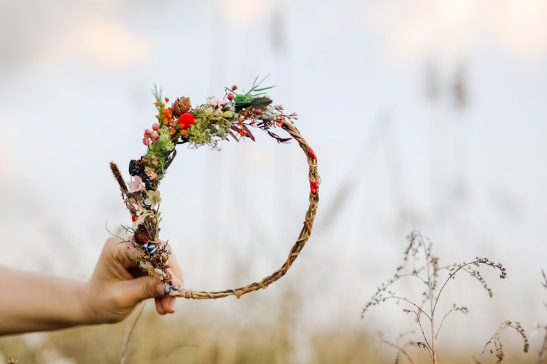 May include: A woven twig wreath with dried flowers and berries, including red, orange, and green accents.