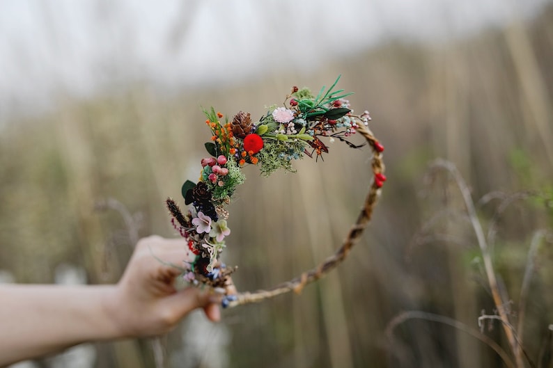 May include: A brown twig headband with a variety of dried flowers and greenery, including red berries, green moss, and small white flowers.