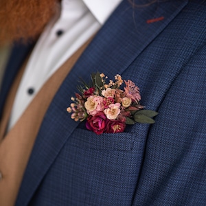 May include: A blue suit jacket with a small bouquet of pink and burgundy flowers pinned to the lapel.