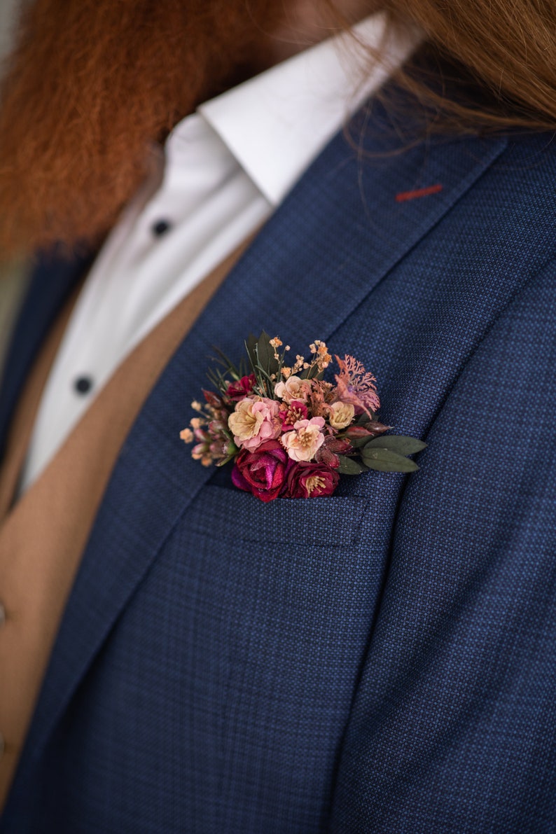 May include: A blue suit jacket with a small bouquet of pink and burgundy flowers pinned to the lapel.