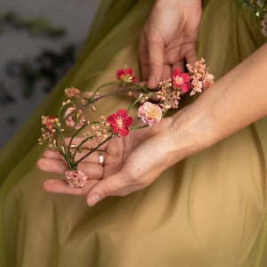 May include: A delicate floral crown with pink and red flowers, woven with thin wire and small green leaves.